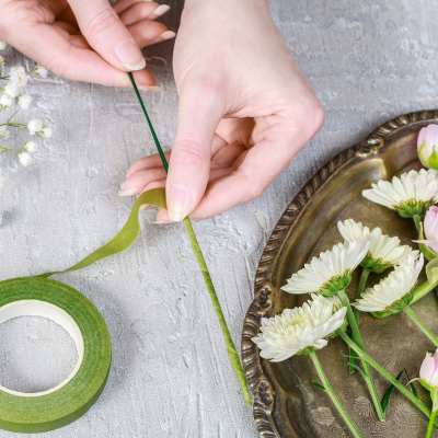 Hands wrapping flower stems with green floral tape beside small white and pink flowers