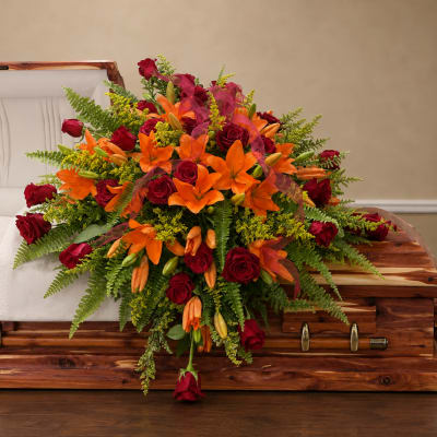 Red roses and orange lilies arranged on a wooden casket
