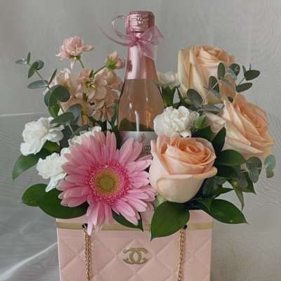 Pink floral arrangement with roses and a champagne bottle in a pink gift bag