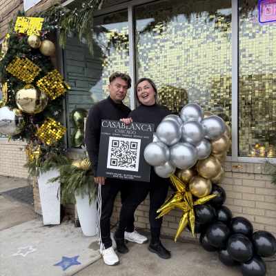Two people stand beside a balloon cluster and holiday storefront decor.