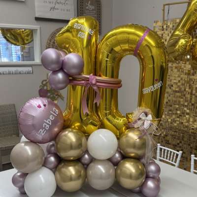 Gold birthday balloon display with pink and lavender accents on a table