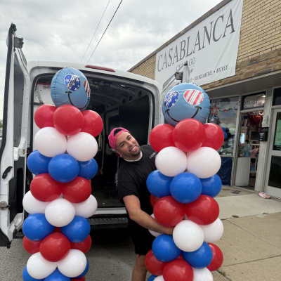 Red, white, and blue balloon columns with smiley-face balloons outside a shop
