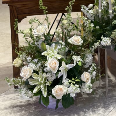 White roses and lilies arranged in a basket with tall white accents