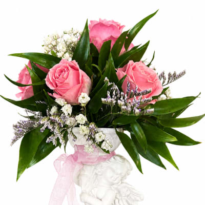 Pink roses and white filler flowers in a white cherub vase with a pink ribbon