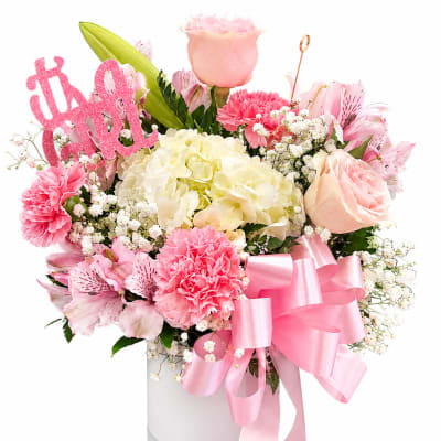 Pink and cream flower arrangement in a glass vase with a ribbon and "it's a girl" sign