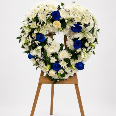 Heart-shaped floral wreath of white flowers with blue roses on a wooden stand