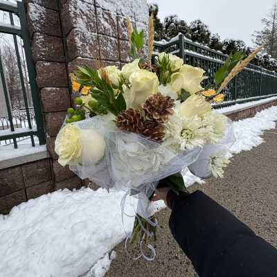 White rose bouquet with pinecones and mesh wrap held outdoors in snow