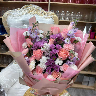Hand-tied bouquet of pink roses, purple mums, and white and pink carnations wrapped in pink paper