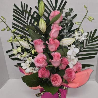 Pink roses and white lilies arranged with palm leaves in a gift box