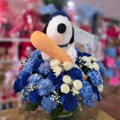 Snoopy plush in a blue flower arrangement holding a toy carrot