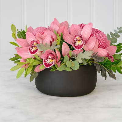 Pink orchid arrangement in a black bowl vase