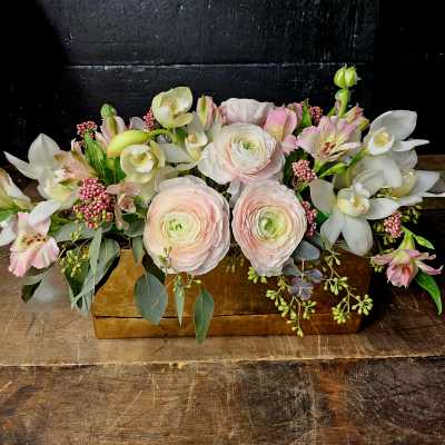 Low floral arrangement with pale pink ranunculus and white orchids in a wooden box