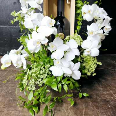 White orchids arranged around a wine bottle in a wooden box