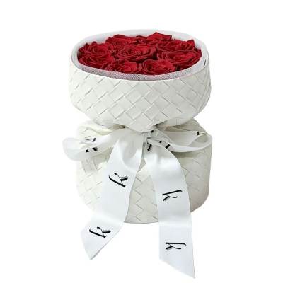 Red roses arranged in a white woven hatbox with a ribbon bow