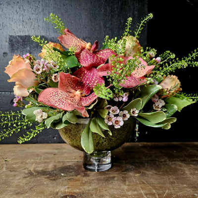 Pink speckled orchids and peach roses in a glass vase