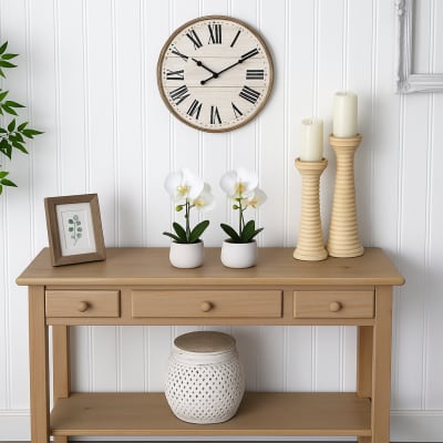 Two white potted orchids on a wooden console with candles and a wall clock