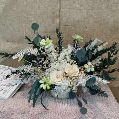 White and cream floral arrangement with dark green foliage in a low vase