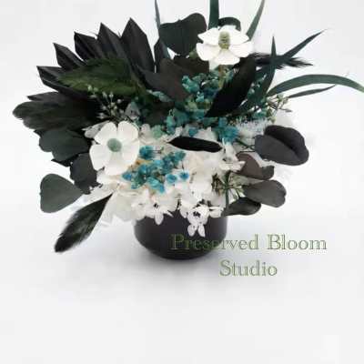 Black and white floral arrangement in a black vase with blue accents