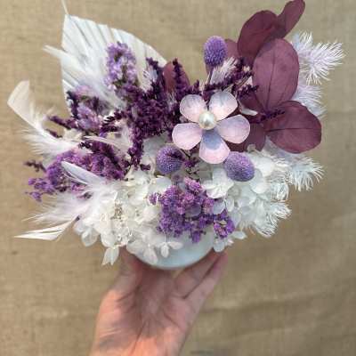 Small purple and white bouquet in a white vase with feather accents