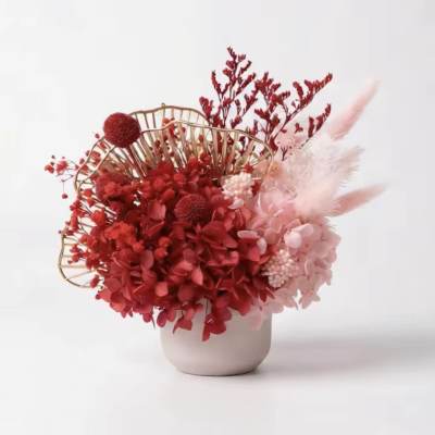 Red and pink floral arrangement in a white vase with gold fan decor