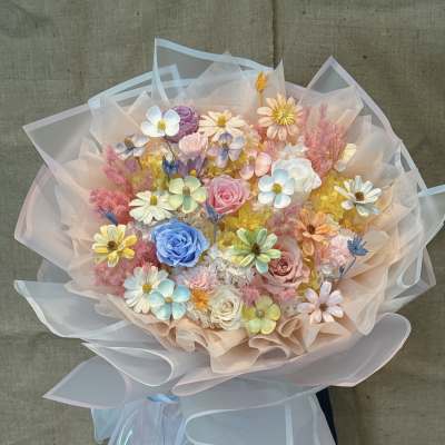 Pastel bouquet of roses and daisy-like flowers wrapped in sheer paper