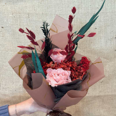 Handheld bouquet of pink roses with red accents and decorative wrap