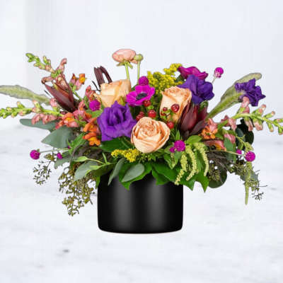Mixed bouquet of peach roses and purple flowers in a black vase