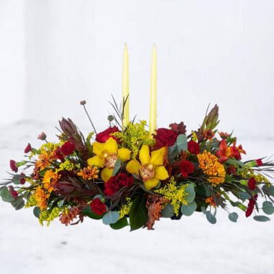 Low floral centerpiece with yellow orchids, red roses, and two tall candles