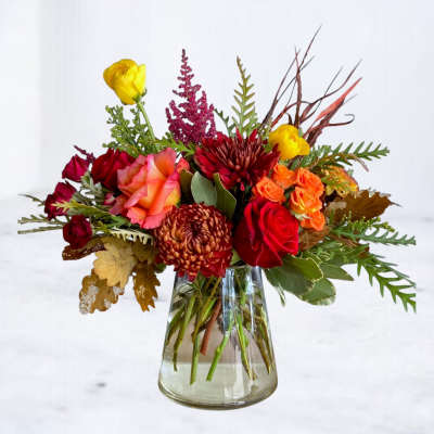 Mixed bouquet of red, orange, and yellow flowers in a clear glass vase