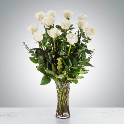 White roses in a tall glass vase with greenery