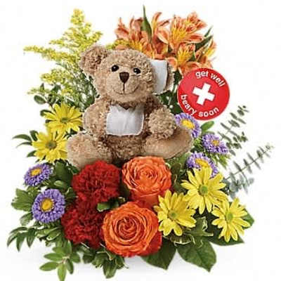 Teddy bear with bandages nestled among bright orange, red, yellow, and purple flowers with a get well sign.
