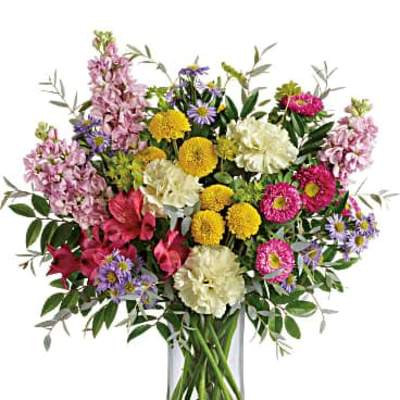Tall mixed bouquet of yellow, pink, purple, and cream flowers in a clear glass vase