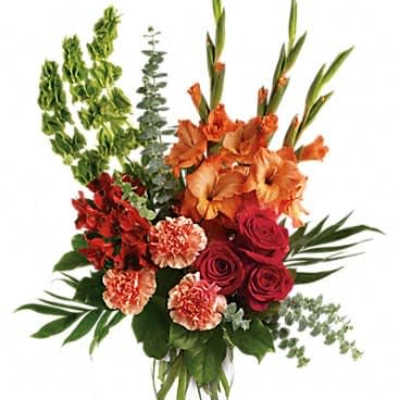 Tall arrangement of orange gladiolus, red roses, and peach carnations in a clear glass vase