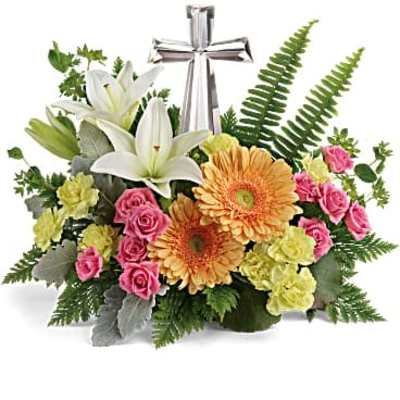 Low arrangement of lilies, gerbera daisies, roses, and carnations around a silver cross.