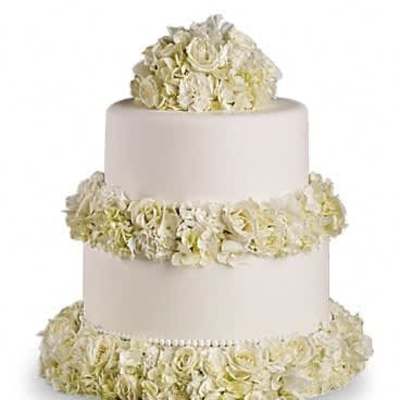 Three-tier white cake encircled with ivory flowers on each layer and topped with a dome of blooms