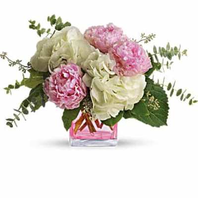 Low arrangement of pink peonies and white hydrangeas in a clear cube vase with pink water