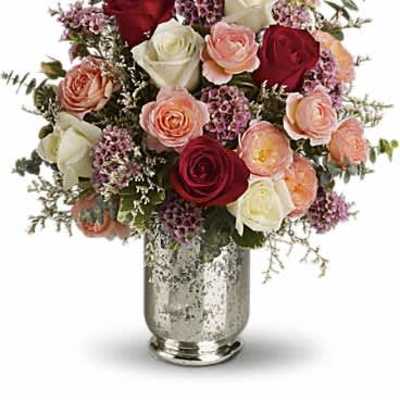 Mixed bouquet of red, white, pink, and peach roses with filler flowers in a silver vase