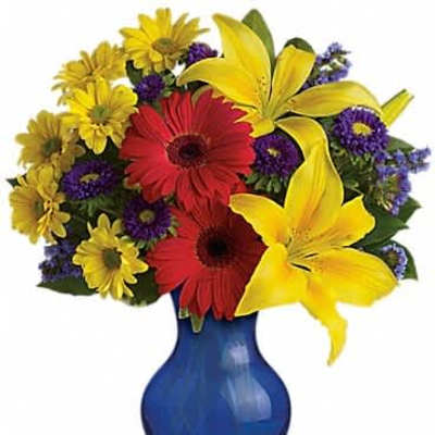 Bright bouquet of yellow lilies, red gerbera daisies, and mixed blooms in a blue glass vase
