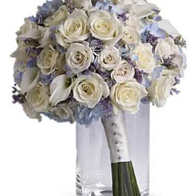 Round bridal bouquet of white roses and calla lilies with pale blue accents in a clear glass cylinder vase