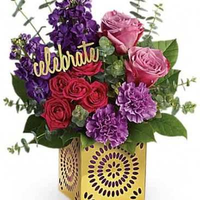 Bright arrangement of pink roses and purple flowers in a yellow cube vase with a celebrate sign
