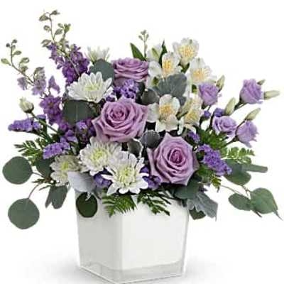 Lavender and white mixed flower arrangement in a white cube vase.