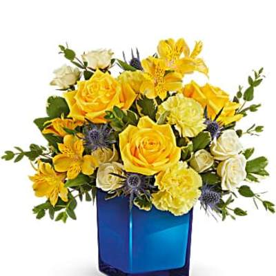 Yellow and cream roses with yellow alstroemeria in a blue glass cube vase
