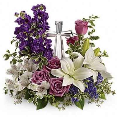 Low purple and white floral arrangement with roses, lilies, and a silver cross in the center