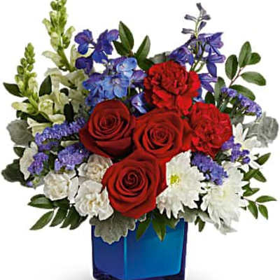Red roses, carnations, and mixed blue and white flowers in a blue glass cube vase