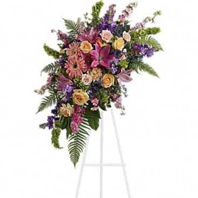 Tall standing spray of pink lilies, gerbera daisies, and peach roses with purple flowers on a white easel