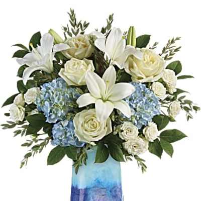 White lilies and roses with blue hydrangeas in a blue ombré glass vase