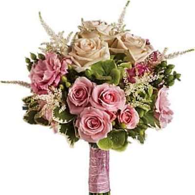 Hand-tied bouquet of cream and pink roses with pink blooms and green accents wrapped in pink ribbon
