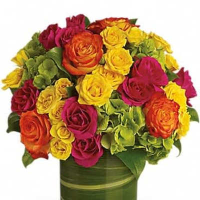 Bright bouquet of orange, yellow, and pink roses with green blooms in a leaf-wrapped glass cylinder vase