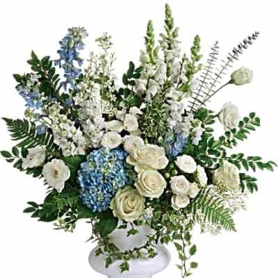 Large white and blue floral arrangement with roses, hydrangeas, and snapdragons in a white pedestal vase
