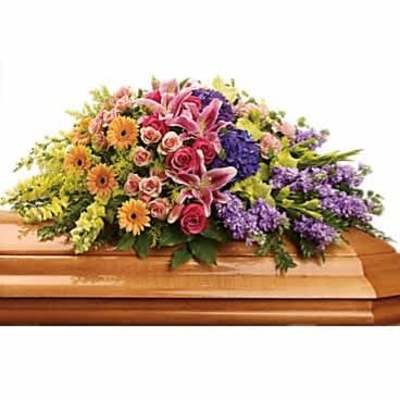 Colorful mixed flower casket spray with pink lilies, roses, and daisies on a wood casket